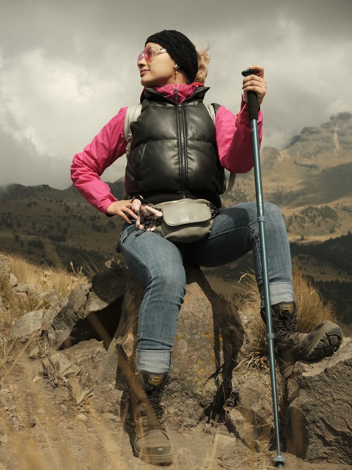 Woman taking a break during a hike in mountainous terrain, wearing warm clothing.