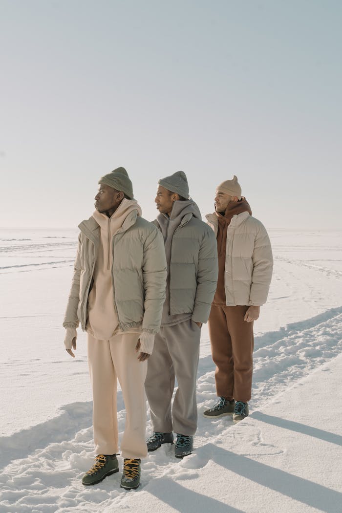 Men in puffer jackets and beanies standing in a snowy landscape showcasing winter fashion.